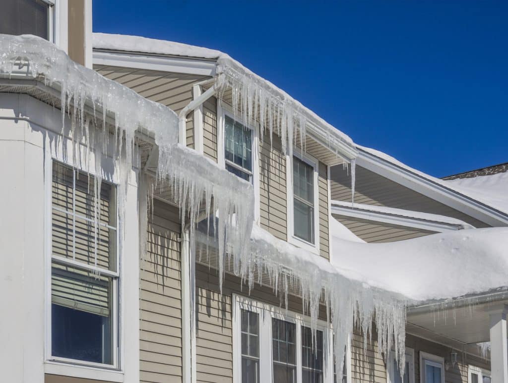 House roof and gutters covered with snow and long icicles hanging from the eaves.